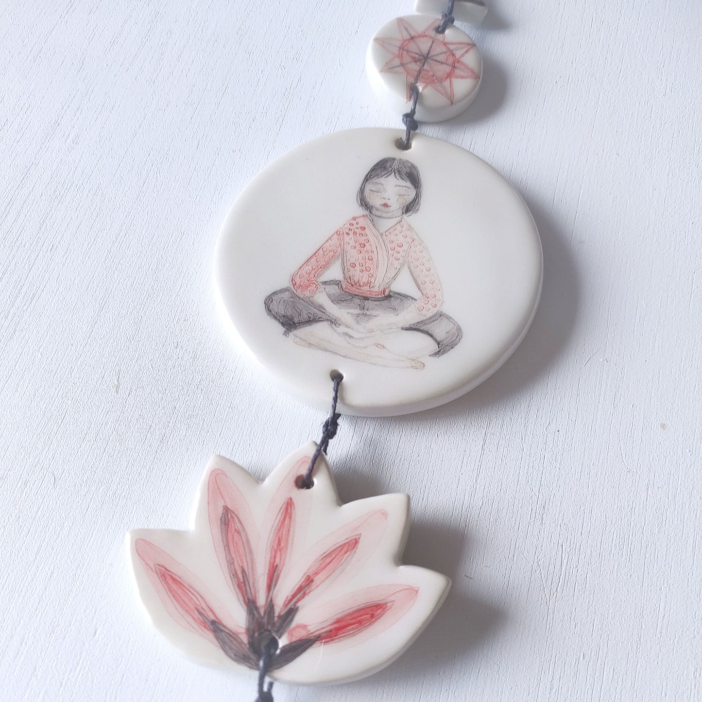 Detalle colgante pared loza esmaltada chica meditación rojo negro BIHU
