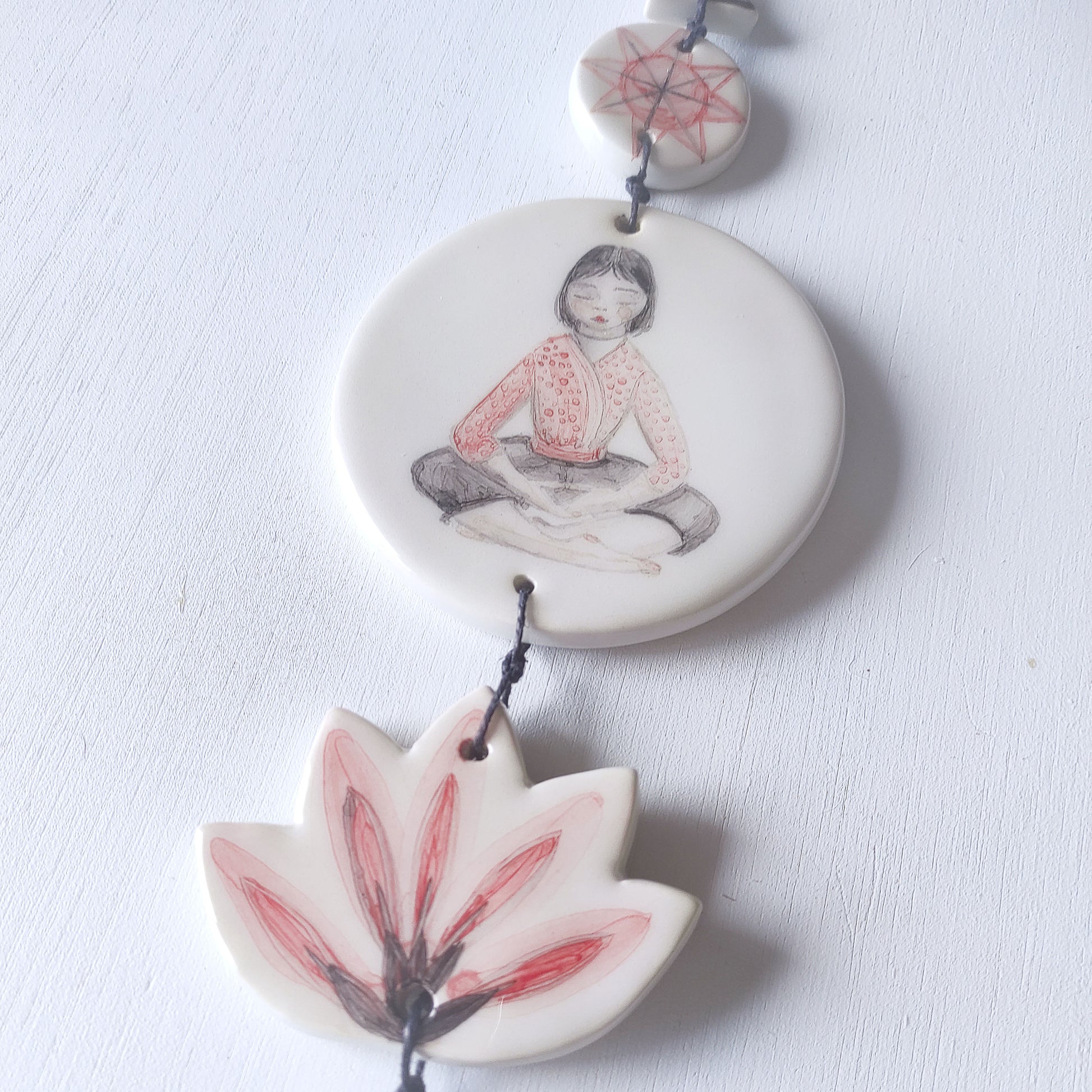 Detalle colgante pared loza esmaltada chica meditación rojo negro BIHU
